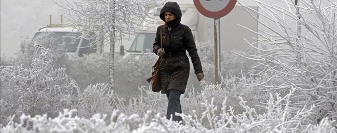 Una mujer camina por la capital vallisoletana, que presenta una imagen blanca con pequeños cristales de hielo similares a la nieve, aunque se trata de gotas de niebla congeladas en su caída.
