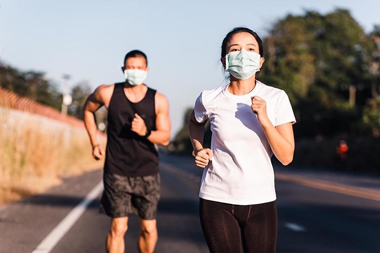 Athletic runner couple wearing face mask while running on street together during Coronavirus or Covid-19 outbreak. Runner couple jogging during quarantine.
