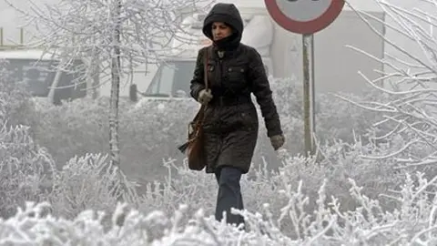 Una mujer camina por la capital vallisoletana, que presenta una imagen blanca con peque&ntilde;os cristales de hielo similares a la nieve, aunque se trata de gotas de niebla congeladas en su ca&iacute;da.
