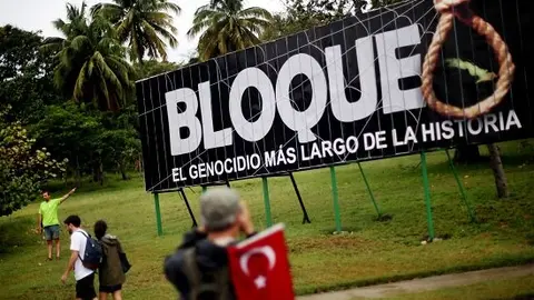 People march by a sign saying, "The embargo: the longest genocide in history," during the 1st of May Labor Day March - a call for people to march in support of their local socialist government and the Cuban Revolution - in Havana, Cuba, on May 01, 2015. The commercial, financial and economic embargo enforced by the United States against Cuba went into effect in 1960, nearly two years after the deposition of the Fulgencio Batista dictatorship by the Cuban Revolution, and just after Cuba nationalized American-owned Cuban properties without remuneration to the States. The embargo at first did not apply to food and medicine, but was quickly broadened to nearly all U.S. exports. Proponents of the embargo cite repeated human rights violations in the country and the appropriated property as reasons to uphold it. Critics define the embargo as too harsh; the UN General Assembly has passed a resolution each year since 1992 criticizing its ongoing impact, citing it to be in violation of the Charter of the UN and international law. In December of 2014, U.S. President Barack Obama signaled an openness in thawing of U.S.-Cuban relations, which started with diplomatic talks and transitioned to the removal of Cuba from the U.S. list of state sponsors of terrorism in May of this year. 