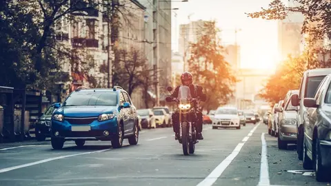 Motorcycle and cars are riding on street. City during the sunset.