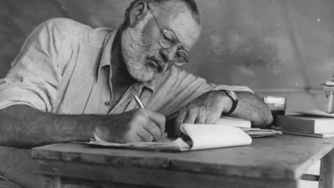 Ernest_Hemingway_Writing_at_Campsite_in_Kenya_-_NARA_-_192655